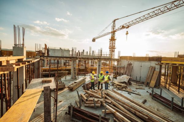 Construction industry concept - architects and engineers discussing work progress between concrete walls, scaffolds and cranes.